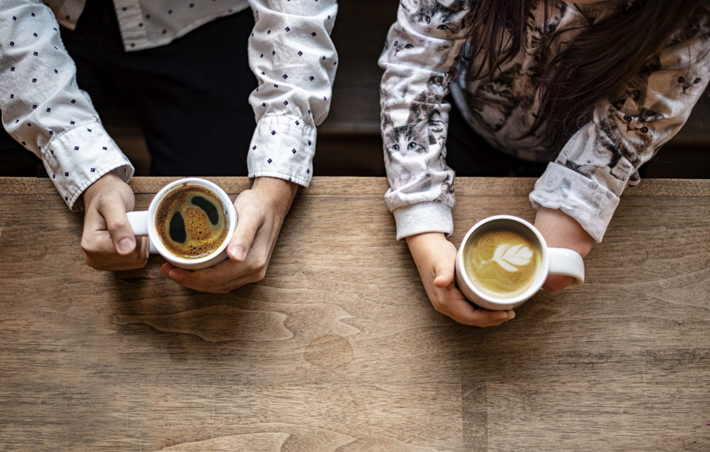 Two cups of coffee on a wooden table, seen from above, two pairs of hands